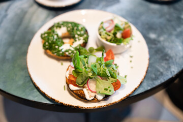 Homemade Breakfast with salmon bagels, radishes, lettuce, tomatoes with garden vegetables, herbs and cream cheese at table in cafe. Healthy or diet food concept