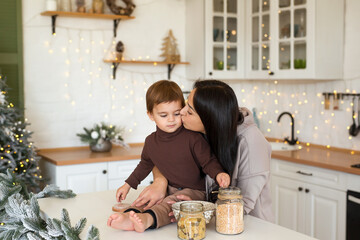 Mom and son playing and having fun at Christmas decorated kitchen. Happy family waiting for the holidays.