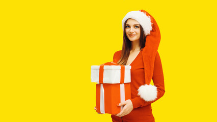 Christmas portrait of happy smiling woman holding gift box in her hands wearing red santa claus hat on yellow background