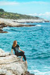 young slim woman sitting on the cliff edge looking at sea