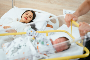 Happy mexican woman after cesarean lying on bed in post natal hospital department. Her husband...