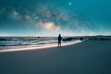 silhouette of a man standing on the shore of the beach looking at the starry sky over the pacific ocean