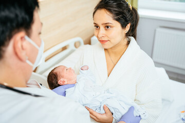 Unrecognizable doctor giving newborn baby boy hispanic woman after birth in postnatal hospital.