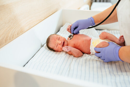 Newborn baby boy in diaper crying during check up examines by pediatrician doctor. Female doctor hand using stethoscope examining little cute baby infant heart, lung in clinic. Health care concept.