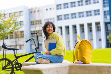 Portrait of a smiling Asian female student sitting in college campus with a bicycle