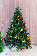 a Christmas tree decorated with colorful balloons, white beads and a glowing electric garland stands in the corner