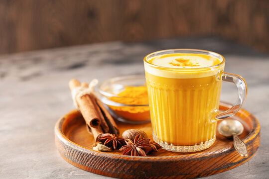 Golden Cinnamon  Turmeric Latte. Trendy hot Healthy drink with turmeric roots and spices. Wooden background