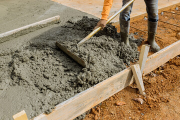 Workers pour cement to create an additional sidewalk to be built on side of house by construction...