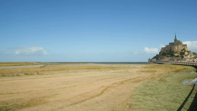 Landscape view of the famous Mont Saint Michel, Normandy, France, during low tide, with the vast colorful coastline. Blue sky with clouds on the background. With copy-space.
