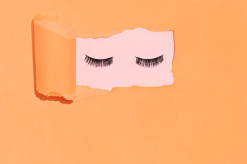 Eye lashes with torn orange paper background. Minimal beauty makeup concept. Creative retro fashion idea.