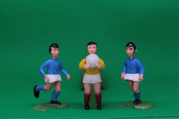 Football Soccer figures in blue and white , with black football boots ,   with goalkeeper in yellow and white with red socks, on green background, vintage soccer action game figures. 