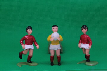 Football Soccer figures in red and white , with black football boots ,   with goalkeeper in yellow and white with red socks, on green background, vintage soccer action game figures. 