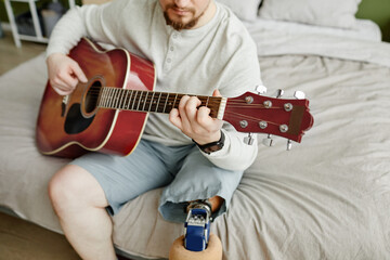 Close up of man with prosthetic leg playing guitar at home, copy space