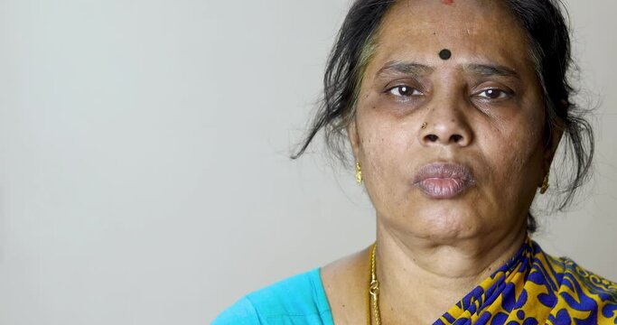 Sad Indian woman standing against white wall at home and looking at camera. A troubled woman with a confused mind.