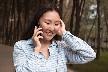 Young happy asian woman talking by phone walking in city park at summer