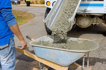Mixer truck pours concrete into wheelbarrow at construction site