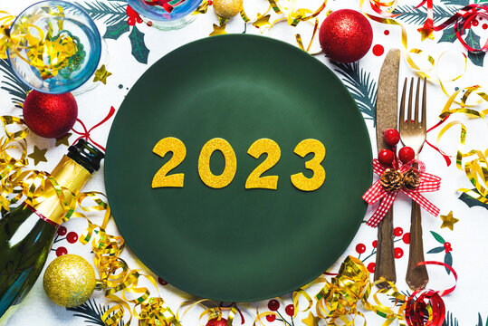Happy new year 2023. Top view of golden Numbers 2023 on plate for Christmas dinner with christmas ornament and champagne bottle . New Years Eve celebration concept background
