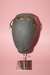Golden royalty crown handmade for a wedding, in a grey mannequin, with a pink background © Julia