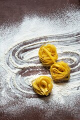 Raw yellow italian pasta (nests) pappardelle, fettuccine or tagliatelle on a brown background,...