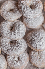 A lot of round donuts with powdered sugar on a cream enameled baking sheet.