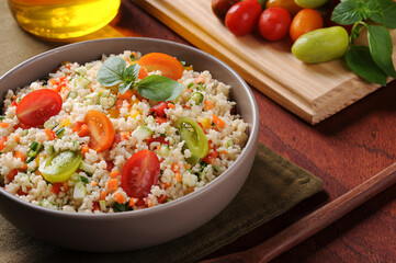 Couscous with vegetables in a rustic bowl surrounded by tomatoes, peppers and a glass of olive oil. Moroccan couscous. Selective focus.