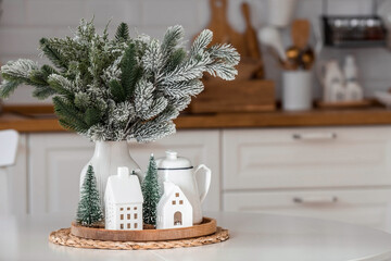 A spruce bouquet and Scandinavian houses on a white kitchen table. Christmas decorations in the...