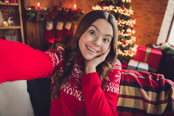 Portrait of impressed excited ecstatic girl with wavy hairdo dressed red ornament sweater making selfie palm on cheekbone in house indoors