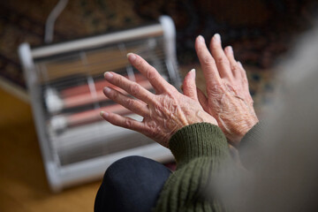 Close Up Of Senior Woman Warming Hands On Electric Heater In Cosyt Of Living Energy Crisis