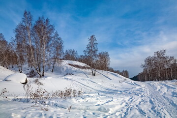 Fototapeta na wymiar Winter landscape with birch trees on the mountain bank of the river, snow and blue sky with clouds