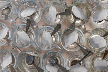 On table is group of empty glass cups with paper tea bags and metal spoons. View from above. Pattern and rhythm.