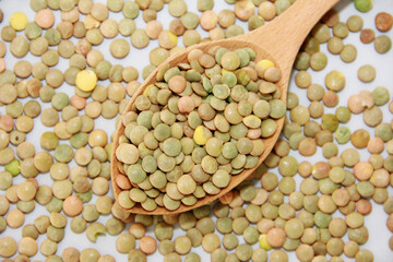 small grains of natural green lentils in a wooden spoon on a gray background