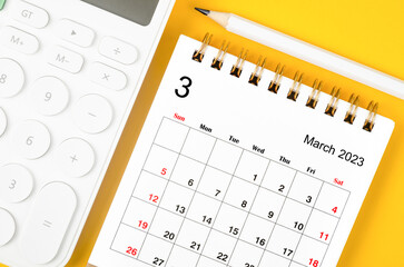 The March 2023 desk calendar for 2023 year with calculator and pencil on yellow background.