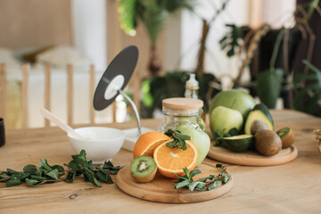 Various ingredients lying at wooden table for preparing natural cosmetics at home. Coconut, orange, mint, avocado, kiwi skin and hair care home spa. Jar of mask and cream.