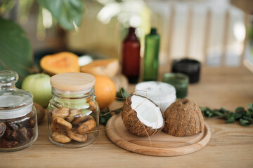 Fototapeta na wymiar Various ingredients lying at wooden table for preparing natural cosmetics at home. Coconut, orange, mint, fig skin and hair care home spa. Jar of mask and cream.