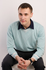 portrait of a seated young man in a blue sweater, on a light background