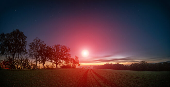 fantastic night landscape with a starry blue sky and red moonlight over a country road