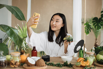 Asian brunette shoulder length hair female social media influencer in bathrobe streaming and...