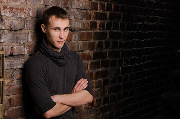 Obraz premium young man in a black jacket against the background of a brown, red and black brick wall