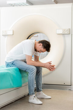 Full Length Of Depressed Man Sitting With Bowed Head Near Computed Tomography Machine.