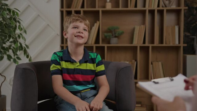 Kid talking to therapist. Practitioner making notes sitting at psychologist office, over the shoulder view. Awareness of children's mental health.