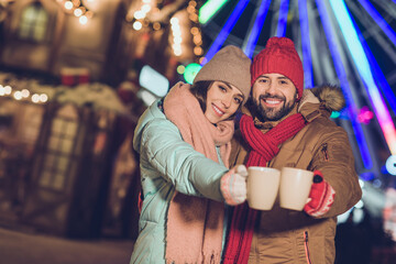 Photo of two lovely peaceful partners embrace hold hot chocolate cup enjoy garland lights x-mas evening outdoors