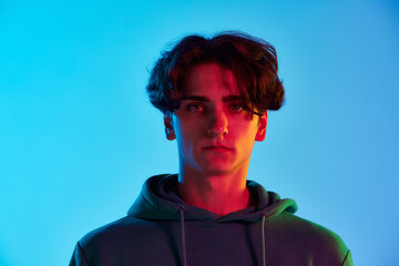 Portrait of young man with curly hair posing, seriously looking at camera isolated over blue...