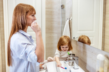 Young mother with a child brushing teeth in the morning. Mother And Daughter Brushing Teeth Together Over Sink. Shot of a woman and her daughter brushing their teeth at home
