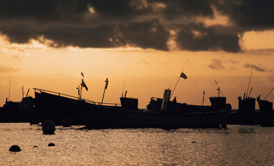 Fototapeta premium Silhouette many fishing ships in harbor on seaside with altostratus clouds in colorful sunrise sky background and reflection on sea surface at morning time