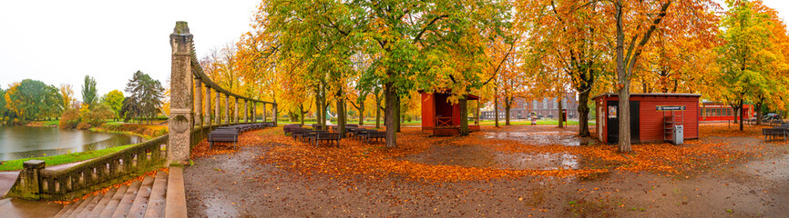 Panorama over lonely empty benches under old chestnut trees and old columns with fallen red and...