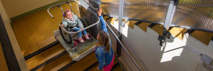 Mother with a young child living with cerebral palsy using electric wheelchair lift to access...