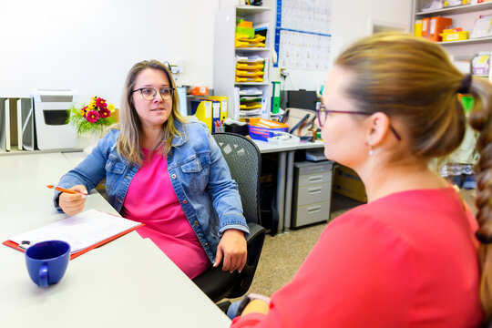 Therapist talking to a young mother after assessing her daughter in complex needs child therapy session.  Two young women talking in an office.
