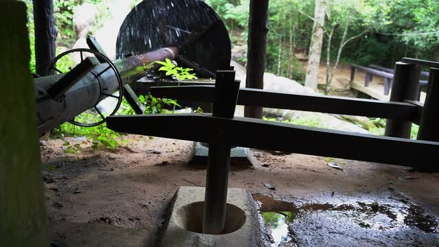 Wooden wheel of an old medieval water mill used for rice production 
 with background of a waterfall and forest.
