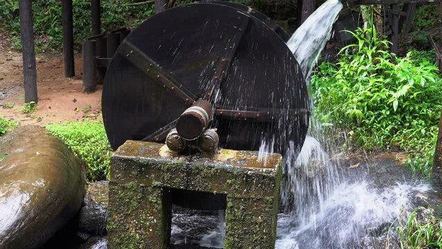 Wooden wheel of an old medieval water mill used for rice production 
 with background of a waterfall and forest.
