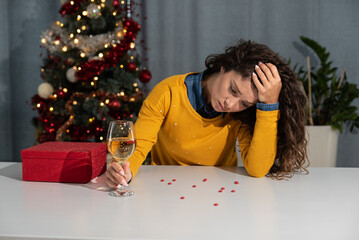 Young business woman sitting alone at home feeling depressed and miserable after relationship breakup divorce at New Year or Christmas Eve. Sad desperate female feeling anxious and abandoned dinking.